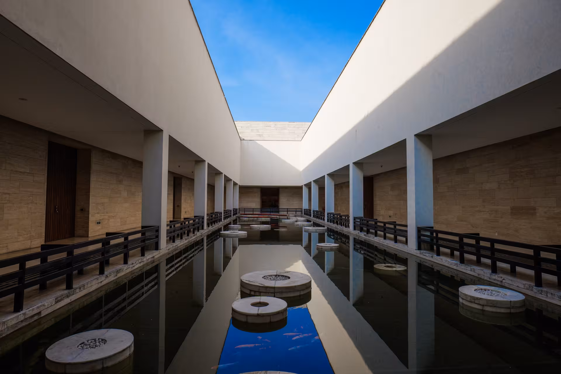 Modern architectural design featuring a reflective water pathway and geometric shapes under a clear blue sky in Hangzhou.