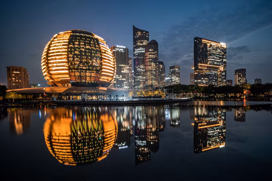 Hangzhou's skyline at night with the illuminated architecture reflecting on the water, showcasing modern innovation.