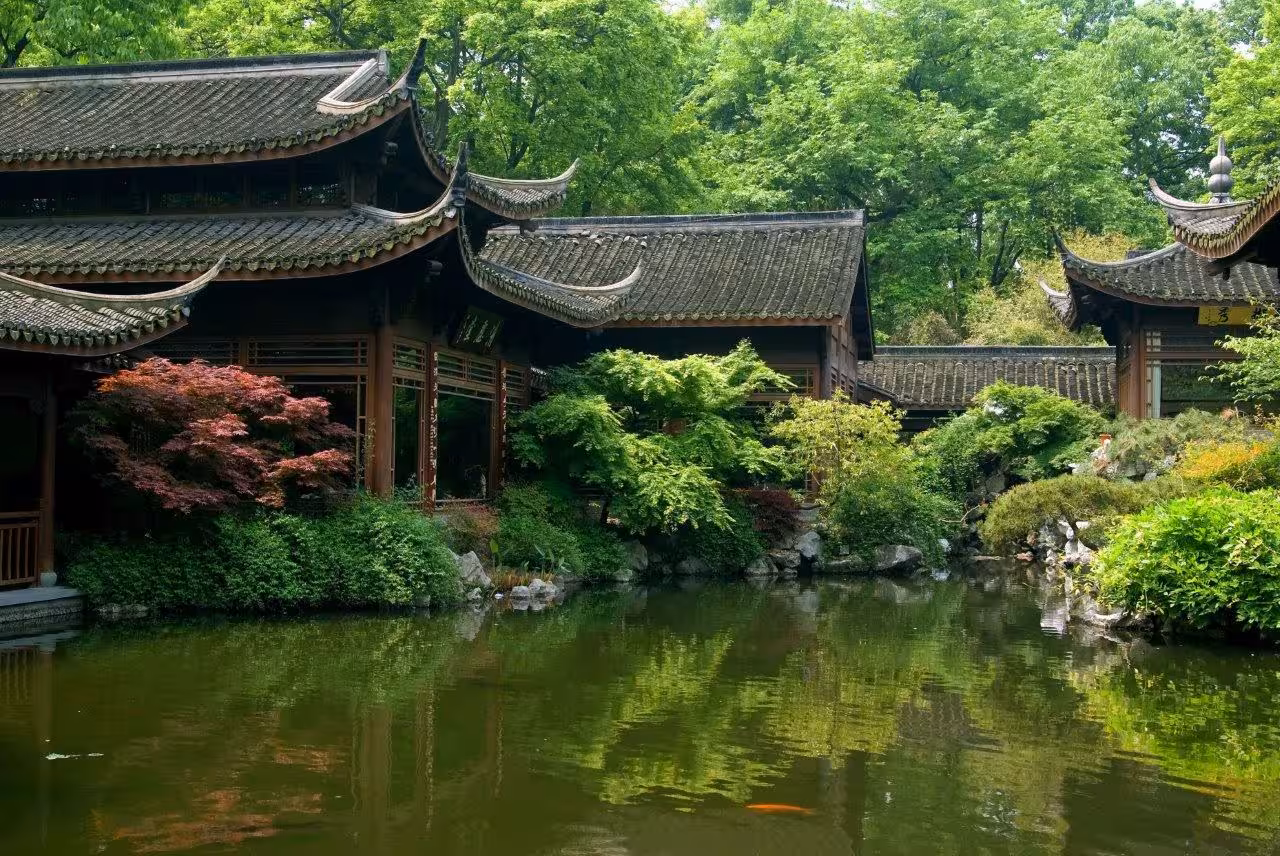 Serene view of traditional Chinese pavilion by a lush garden pond in Hangzhou, ideal for ancient healing and heritage tours.