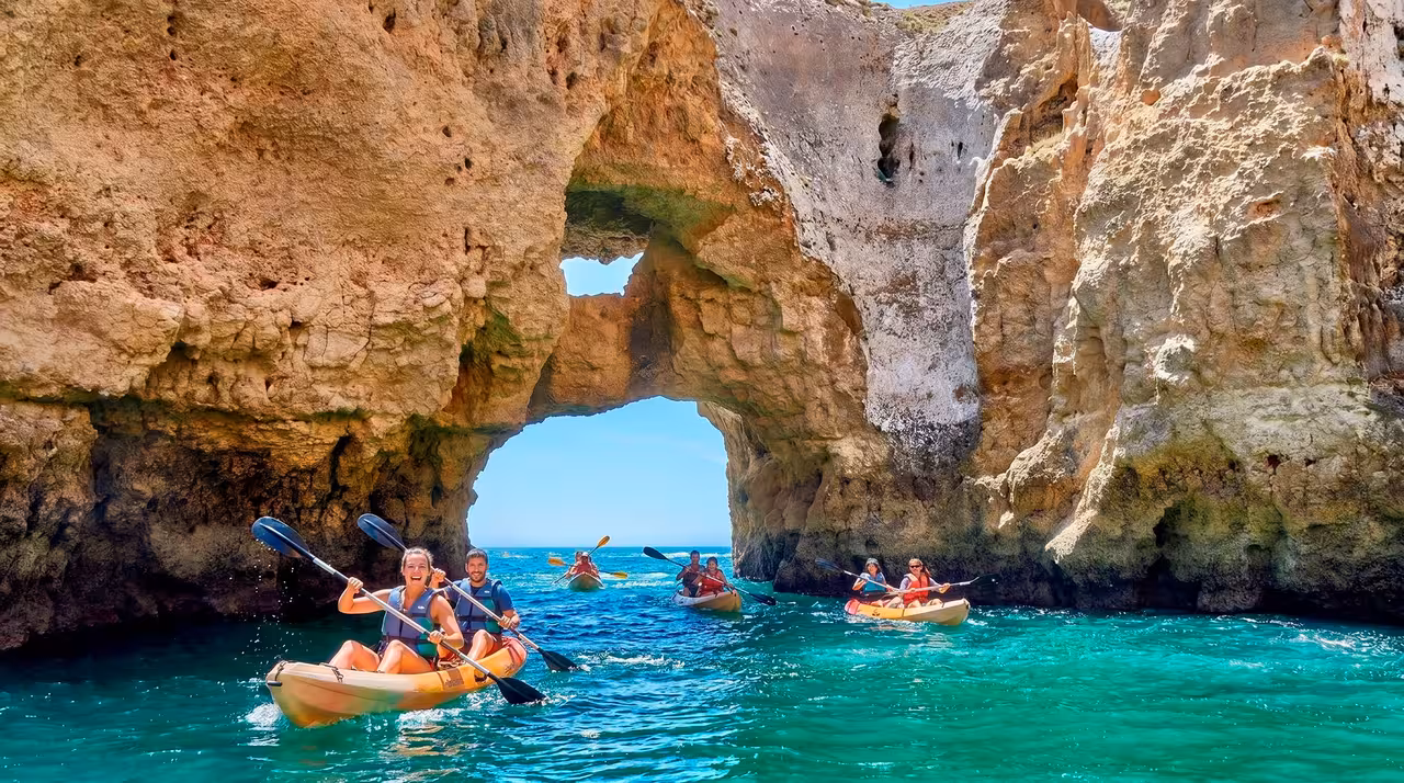 Smiling kayakers exploring turquoise waters inside scenic Ponta da Piedade rock arch caves Lagos Portugal
