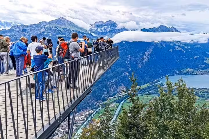 Tourists enjoy breathtaking views from the Harder Kulm observation deck overlooking mountains and valleys in Switzerland.