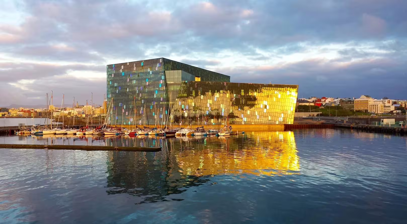 Harpa Concert Hall with colorful glass facade reflecting golden light on Reykjavik harbor at sunset