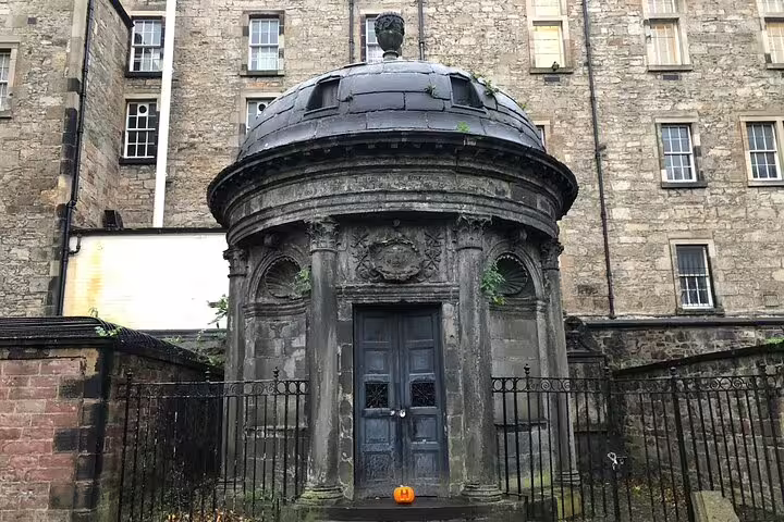 Ancient stone mausoleum with domed roof in Edinburgh graveyard, decorated with Halloween pumpkin
