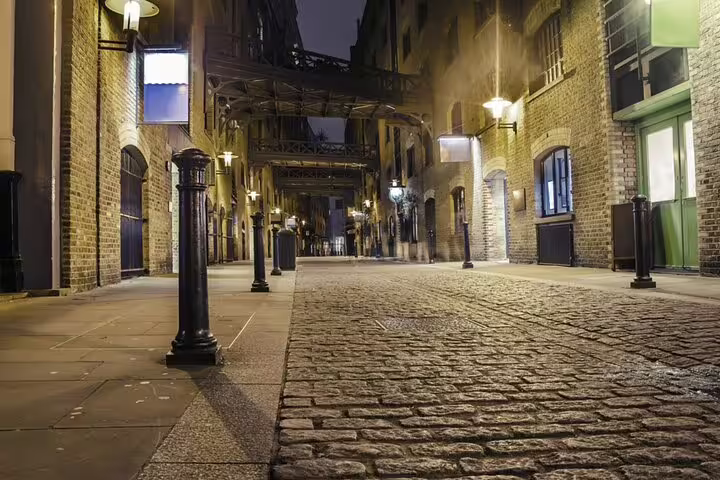 Dimly lit cobblestone street at night flanked by Victorian brick buildings in London