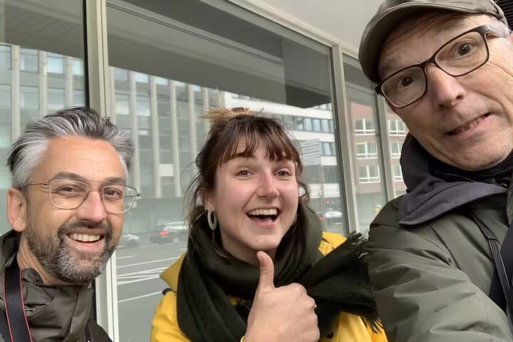 Three smiling people on a self-guided walking tour in Cologne, one giving a thumbs up