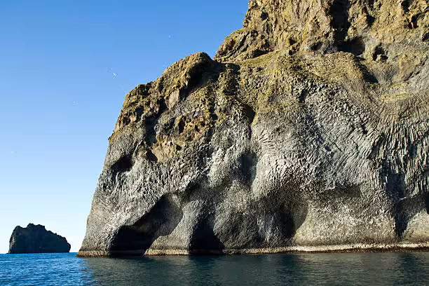 Rocky sea cliffs with cave arches at Westman Islands Heimaey, viewed from boat on calm blue water