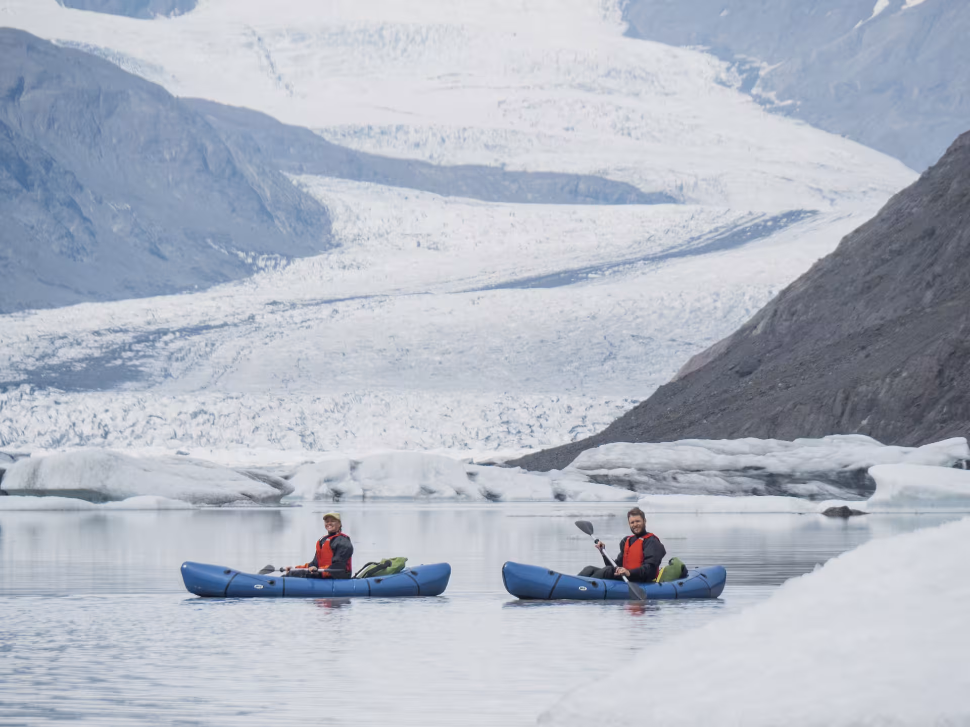 Two kayakers paddling Heinabergslón glacier lagoon with Vatnajökull ice backdrop on a guided kayak and hike tour