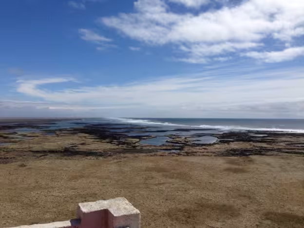 Coastal lava fields and tidal pools with ocean waves under blue sky near volcanic landscape