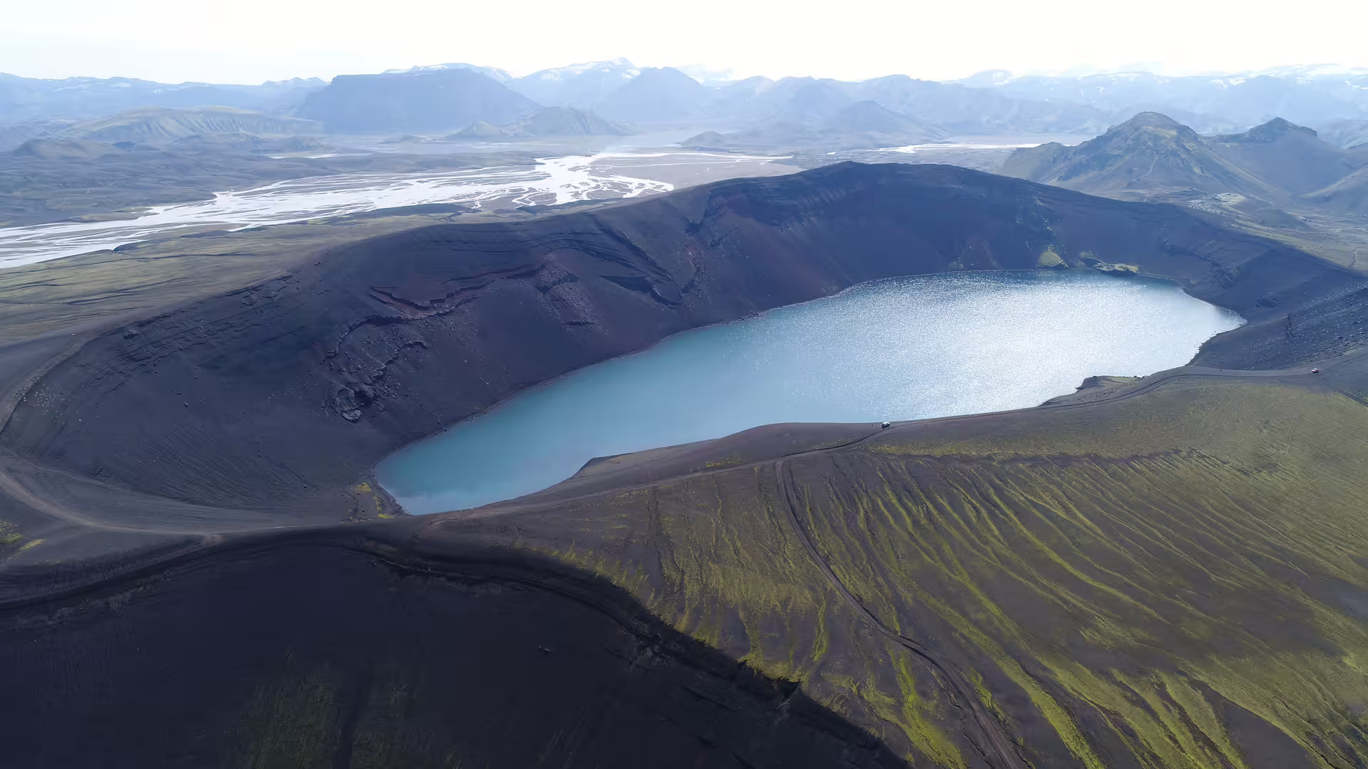 Aerial view of a volcanic crater lake with dark lava terrain and braided glacial rivers in Iceland's highlands