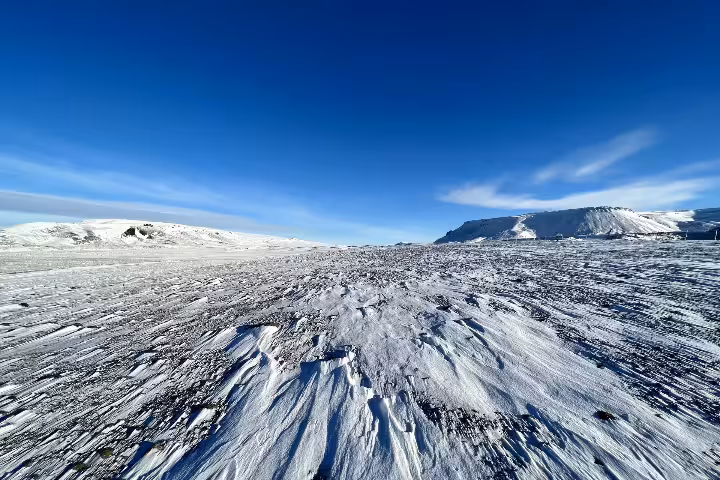 Wind-swept glacier surface with dark volcanic ash streaks near Hekla volcano under a clear blue sky
