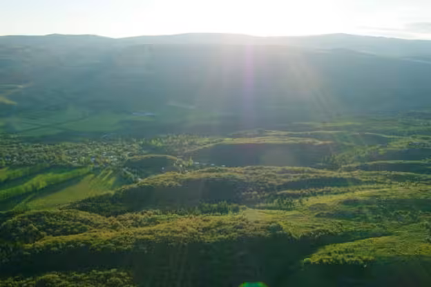 Aerial view of lush green volcanic highlands with sunburst over rolling hills and small village below