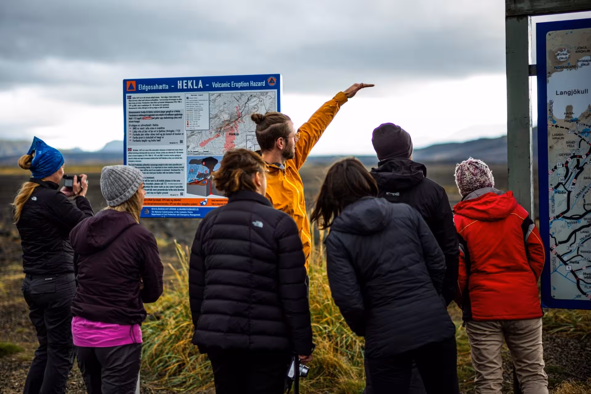 Tour guide pointing at Hekla volcanic eruption hazard sign with group of tourists in Iceland highlands