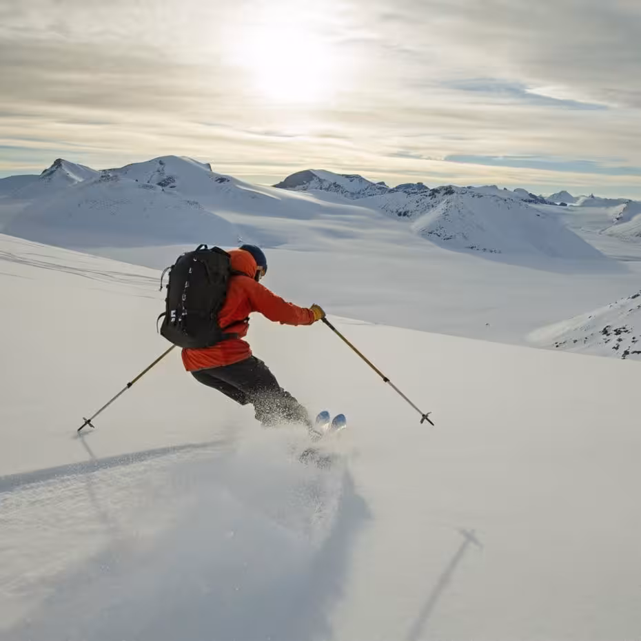 Skier in red jacket carving powder snow on open mountain slopes during heli skiing in Iceland