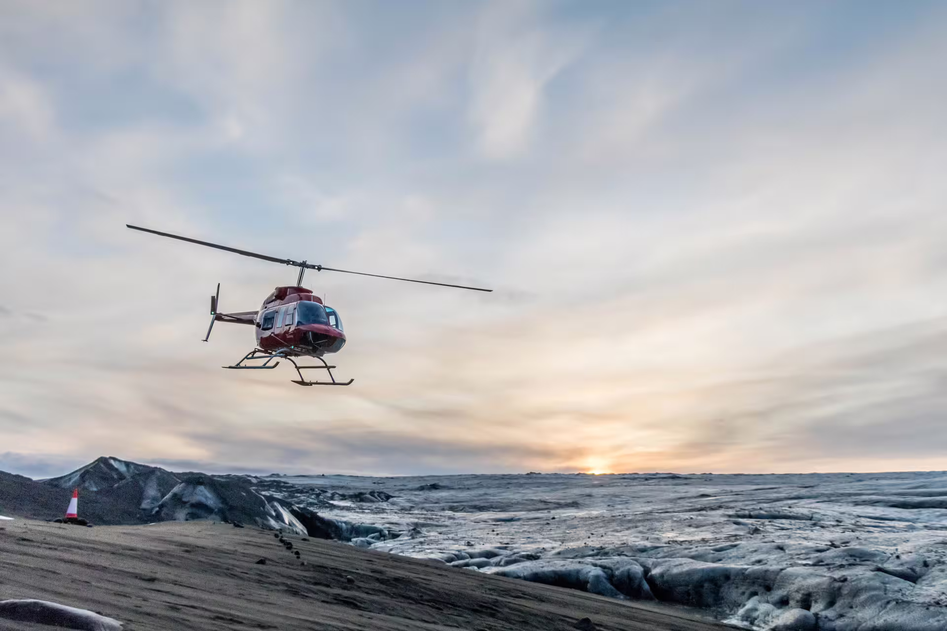 Red helicopter flying low over Vatnajokull glacier in Iceland at sunset