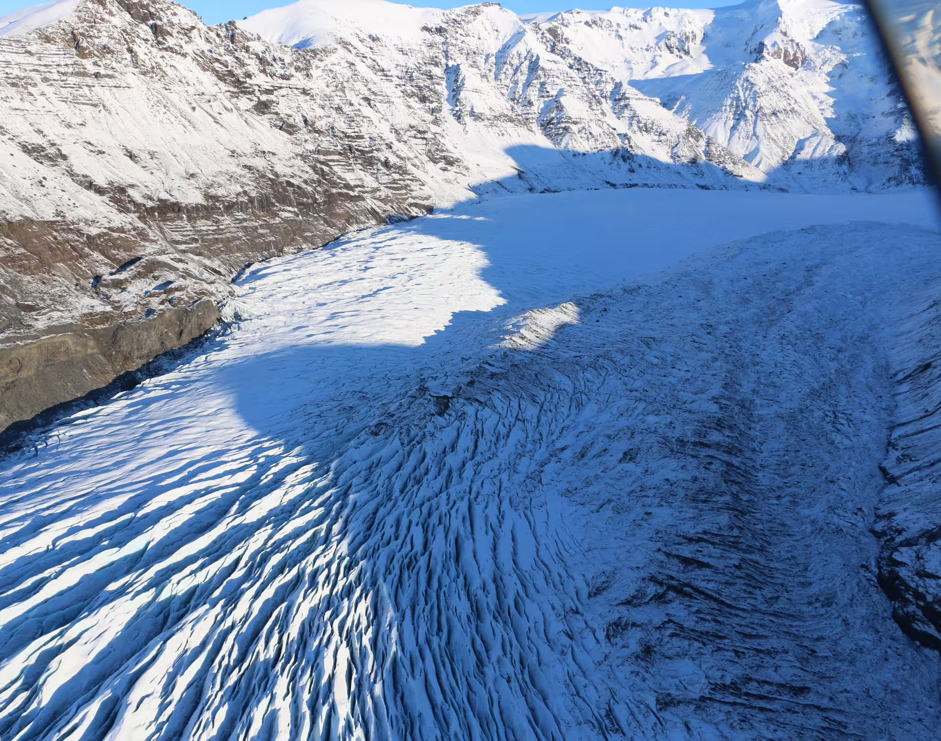 Aerial view of crevassed glacier flowing between snow-covered mountains at Skaftafell, Iceland