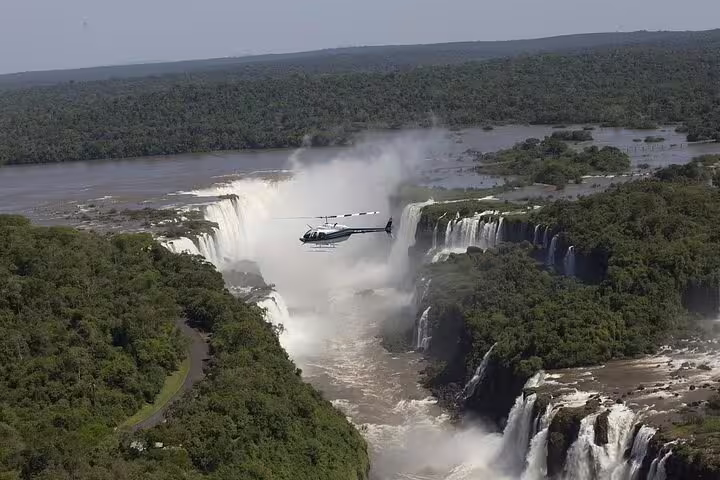 Helicopter soaring over the majestic Iguazu Falls, showcasing breathtaking aerial views of lush greenery and cascading water.