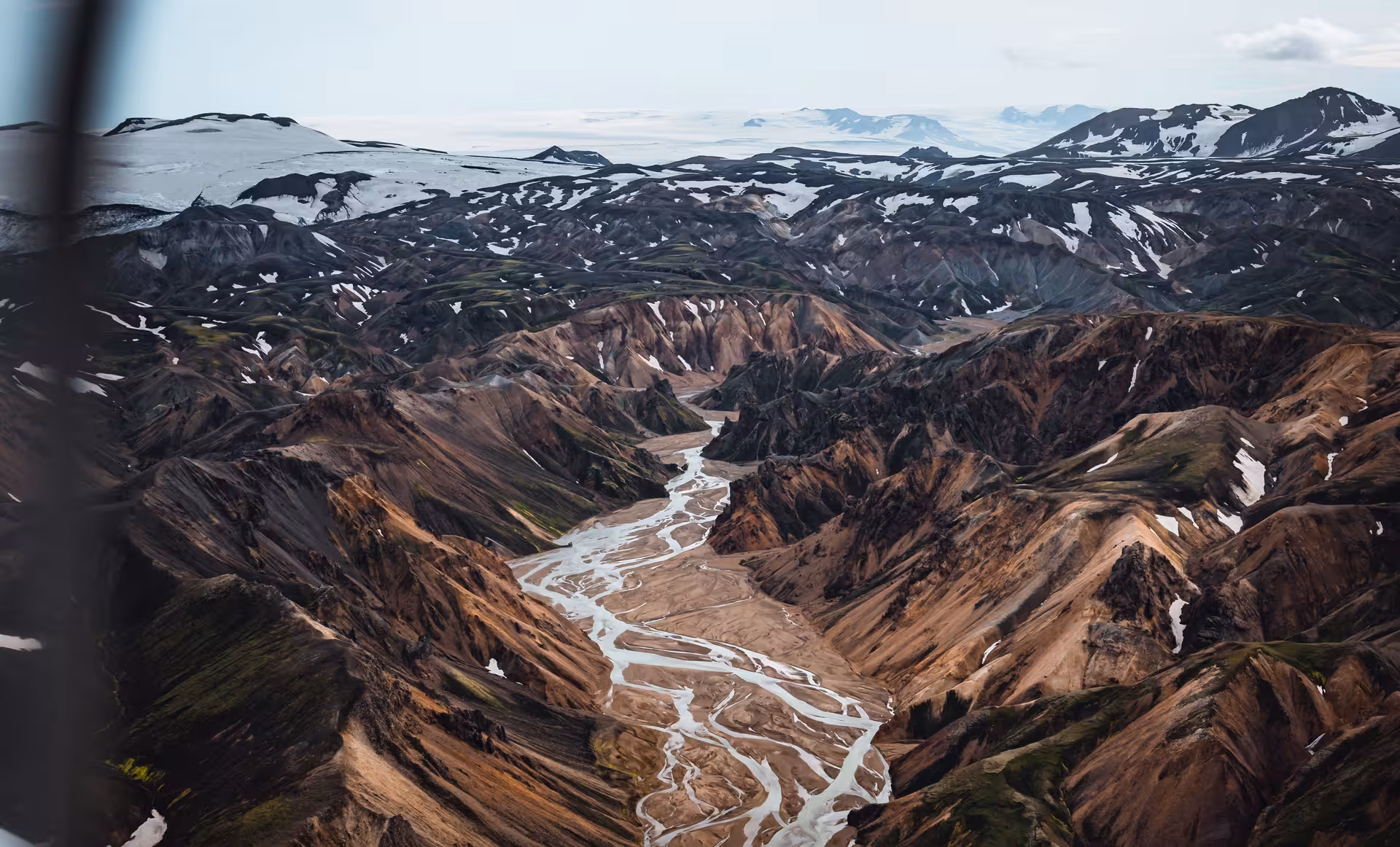 Aerial view of braided glacial river winding through rugged Icelandic highlands with snow-capped mountains
