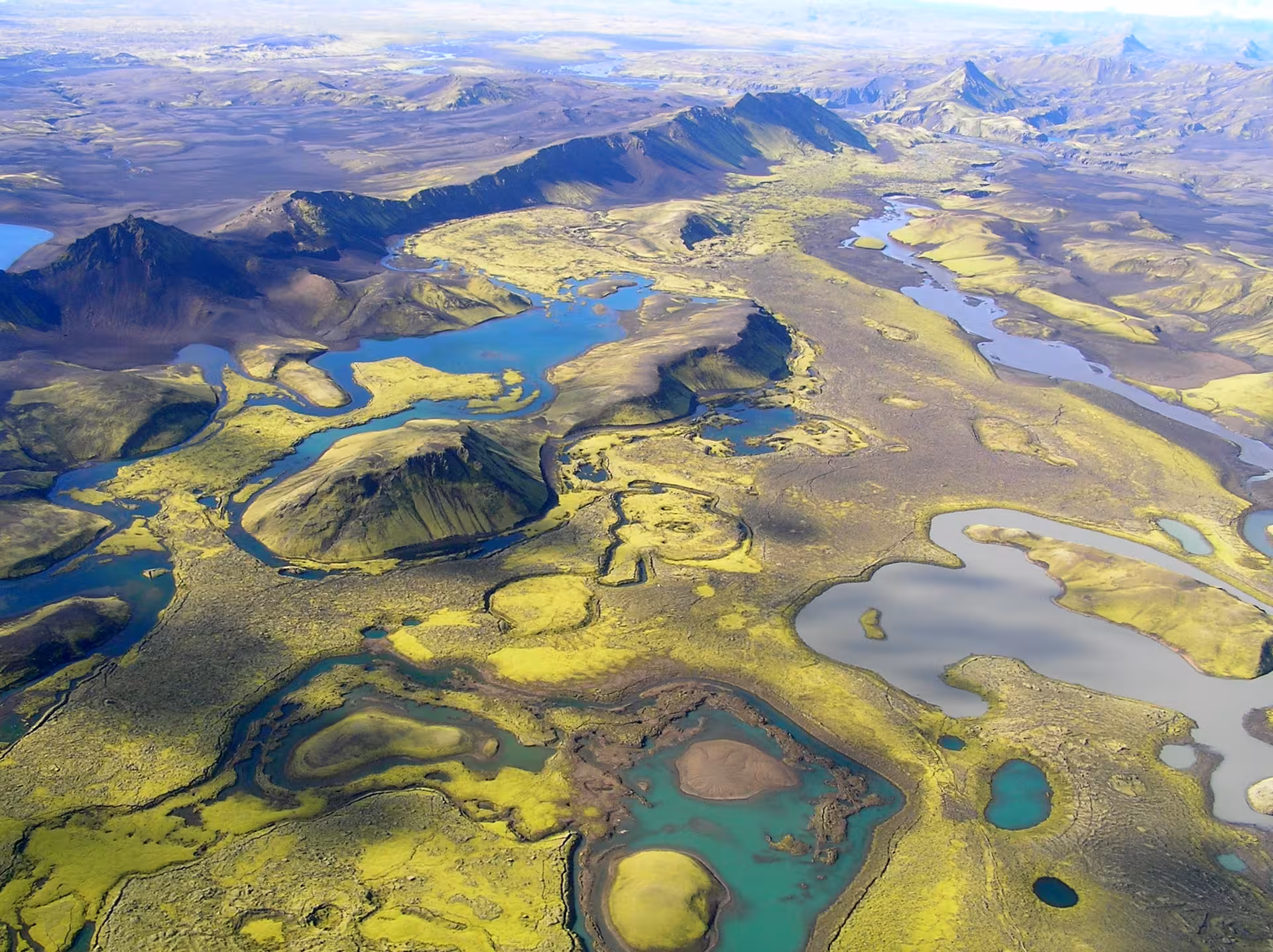Aerial view of Iceland's highland wilderness with winding glacial rivers, turquoise lakes, and volcanic mountains from helicopter