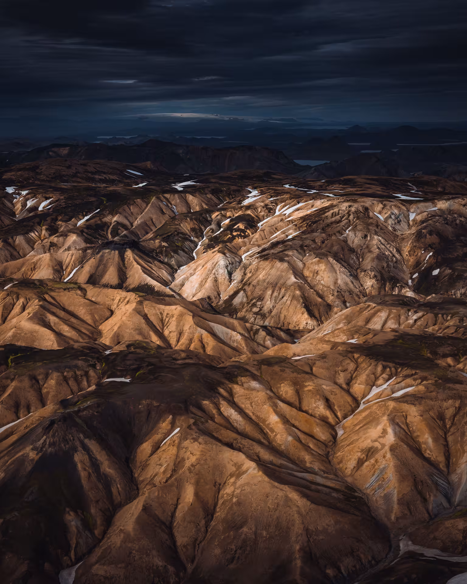 Aerial view of rugged Icelandic highland terrain with snow patches under dramatic dark sky
