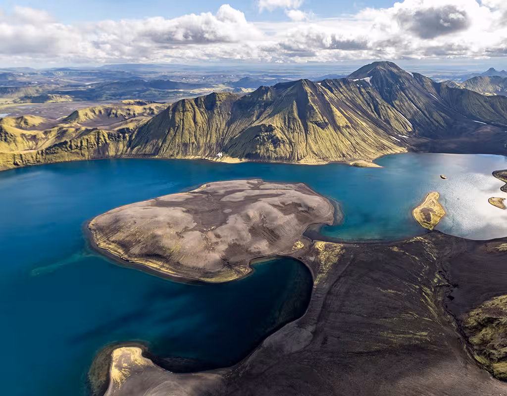 Aerial view of volcanic crater lake with turquoise water and green mountains in Iceland's highlands