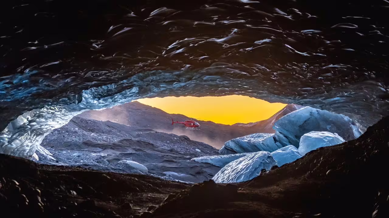 Red helicopter hovering outside a glacial ice cave in Vatnajokull Iceland at golden sunset