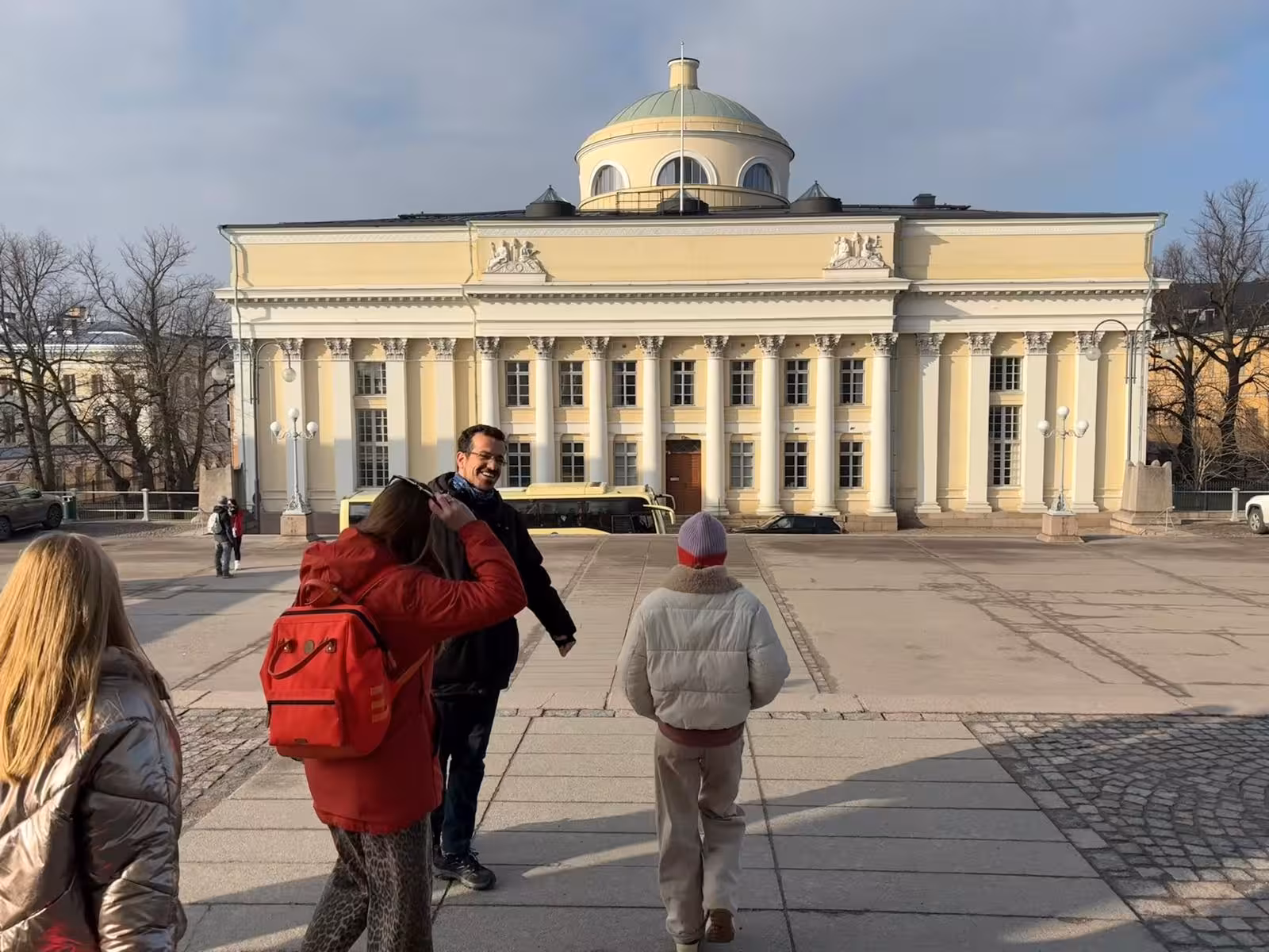Tourists exploring the neoclassical architecture of Helsinki University Library on a sunny day.
