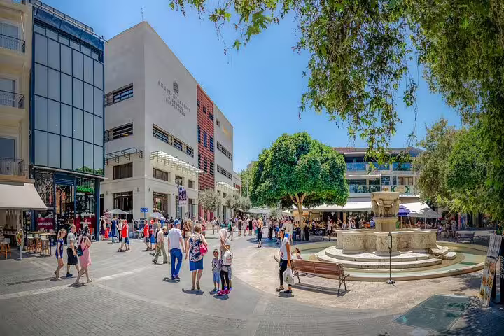 Lively square in Heraklion with bustling crowds, modern architecture, and a historic fountain, a hub for cultural exploration.