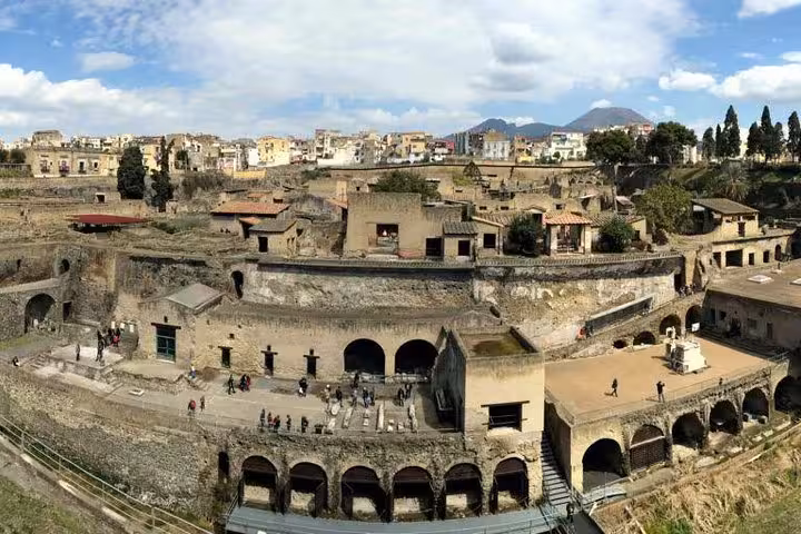 A panoramic view of Herculaneum's archaeological site with Mt. Vesuvius visible in the distance, perfect for history enthusiasts.