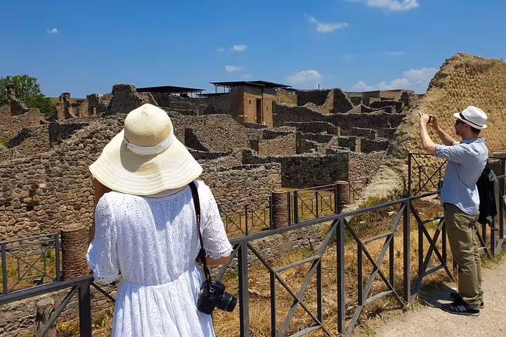 Tourists enjoy capturing the historic ruins of Herculaneum on a sunny day, part of a skip-the-line cultural tour.