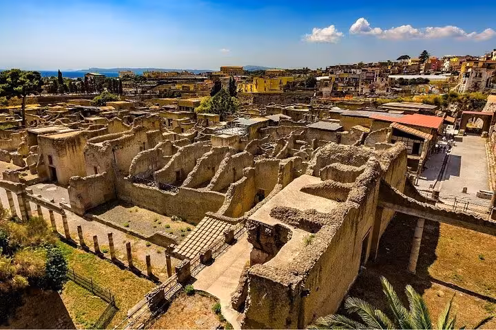 Aerial view of Herculaneum ruins under a clear blue sky, part of a guided tour with lunch and ticket included.