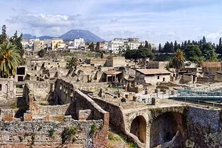 Panoramic view of Herculaneum ruins with Mount Vesuvius in the background, highlighting historical significance.