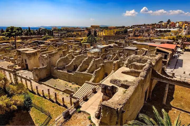 Panoramic view of Herculaneum ruins with detailed ancient architecture against a backdrop of the Italian coastline.