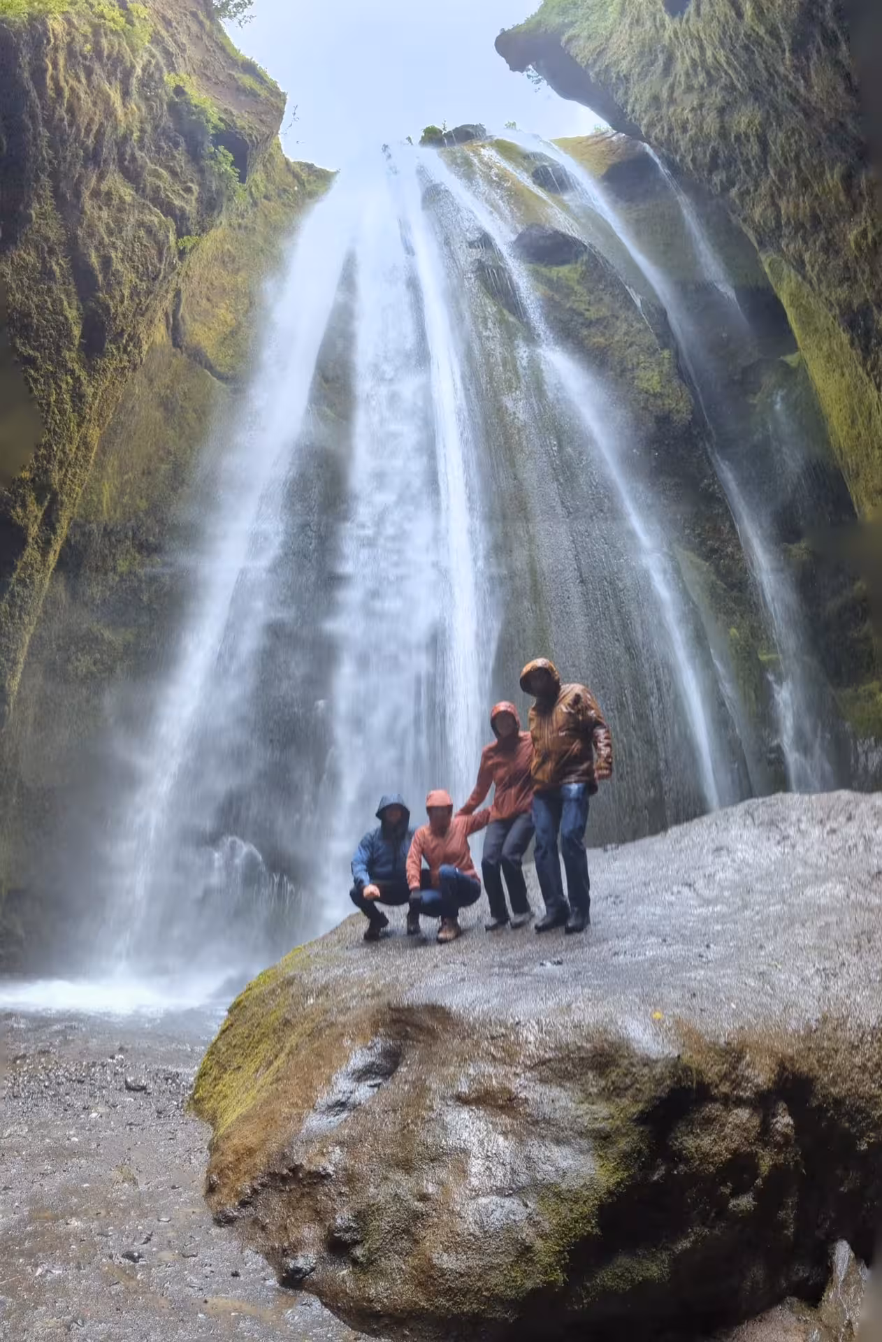 Four tourists in rain gear posing inside Gljúfrabúi canyon waterfall near Eyjafjallajokull Iceland