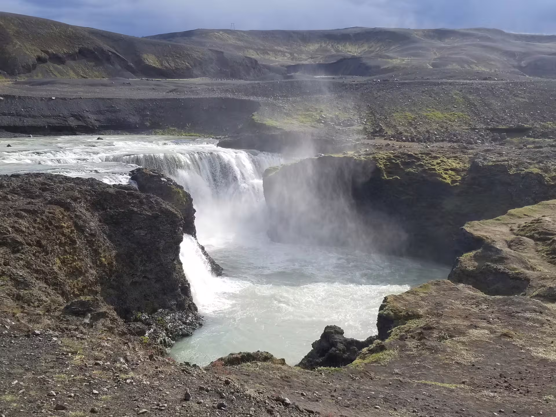 A hidden Iceland waterfall cascading into a misty turquoise pool surrounded by volcanic rock on a private super jeep day trip.