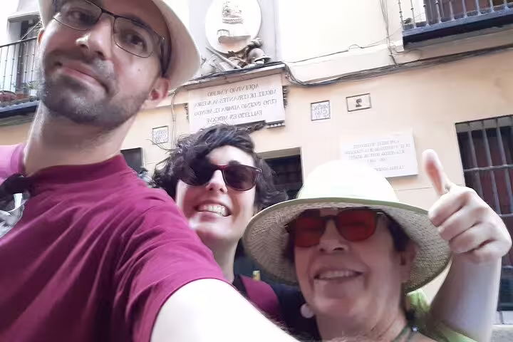 Three smiling tourists taking a selfie in front of a historic Madrid building with plaques