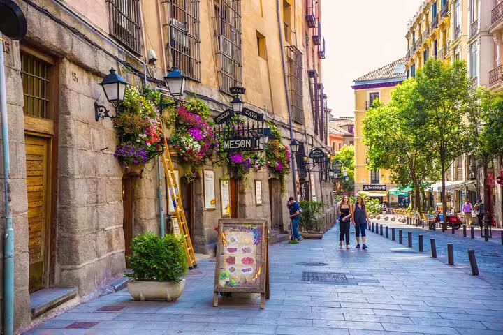 Charming pedestrian street in Madrid with flower-adorned stone buildings and a Meson restaurant sign