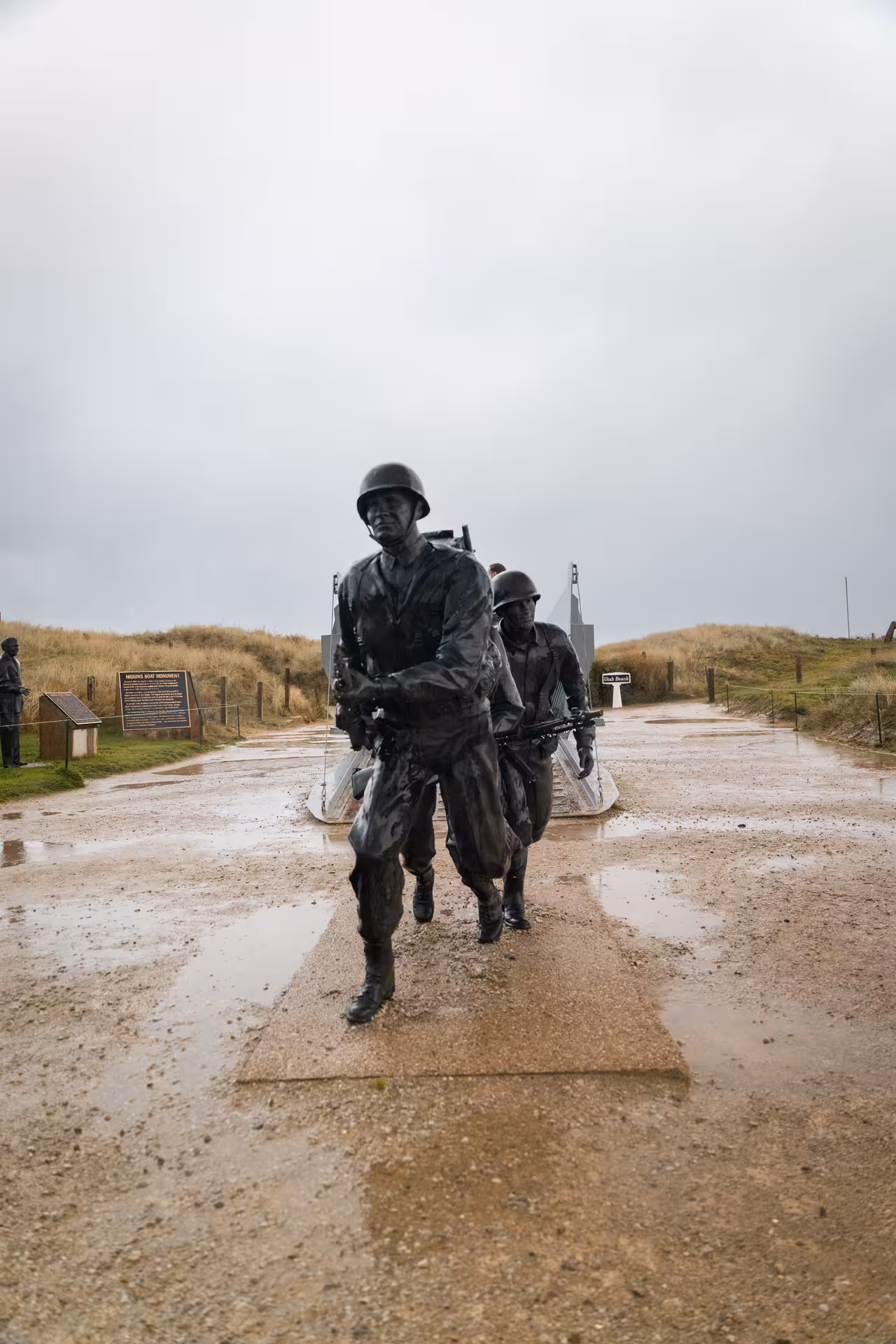 Bronze soldier statues at Higgins Boat Monument on Normandy D-Day landing beach on a rainy day