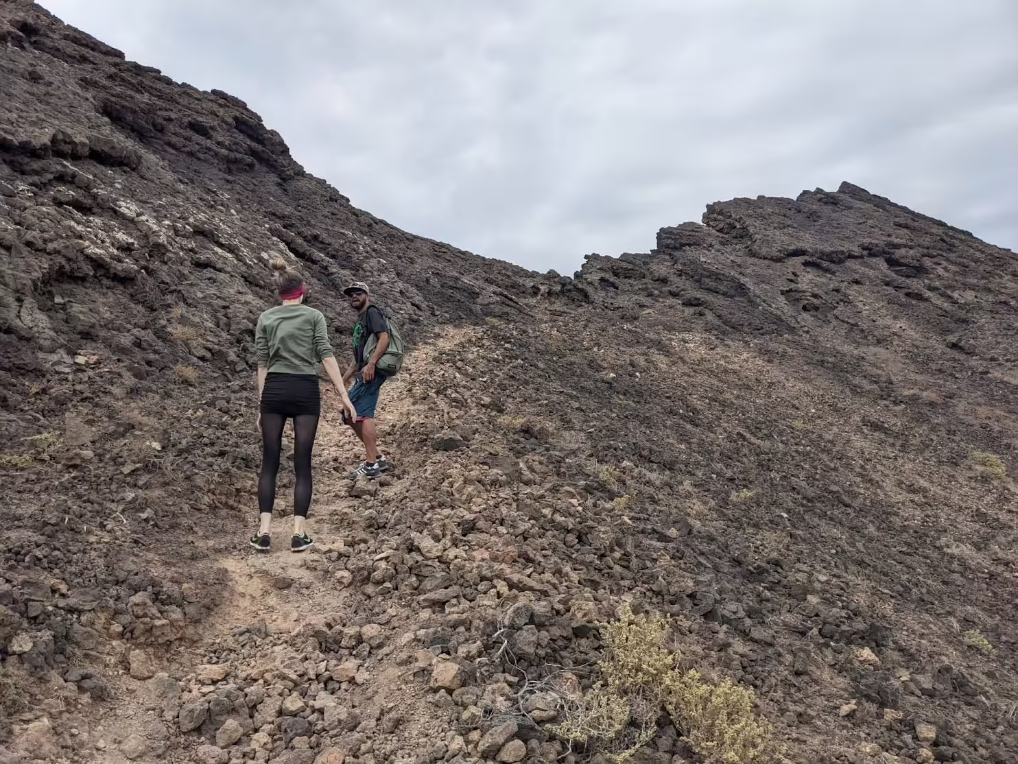 Hikers explore the rugged volcanic terrain of Volcano Viana, São Vicente, under an overcast sky, showcasing adventure travel.
