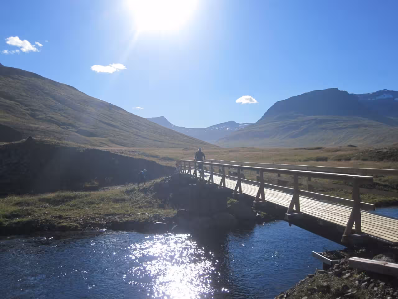 Hiker crossing wooden bridge over glacial river in East Iceland remote fjords on guided trekking tour