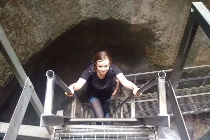 Woman climbing metal stairs out of Seven Ladders Canyon narrow rock passage in Brasov
