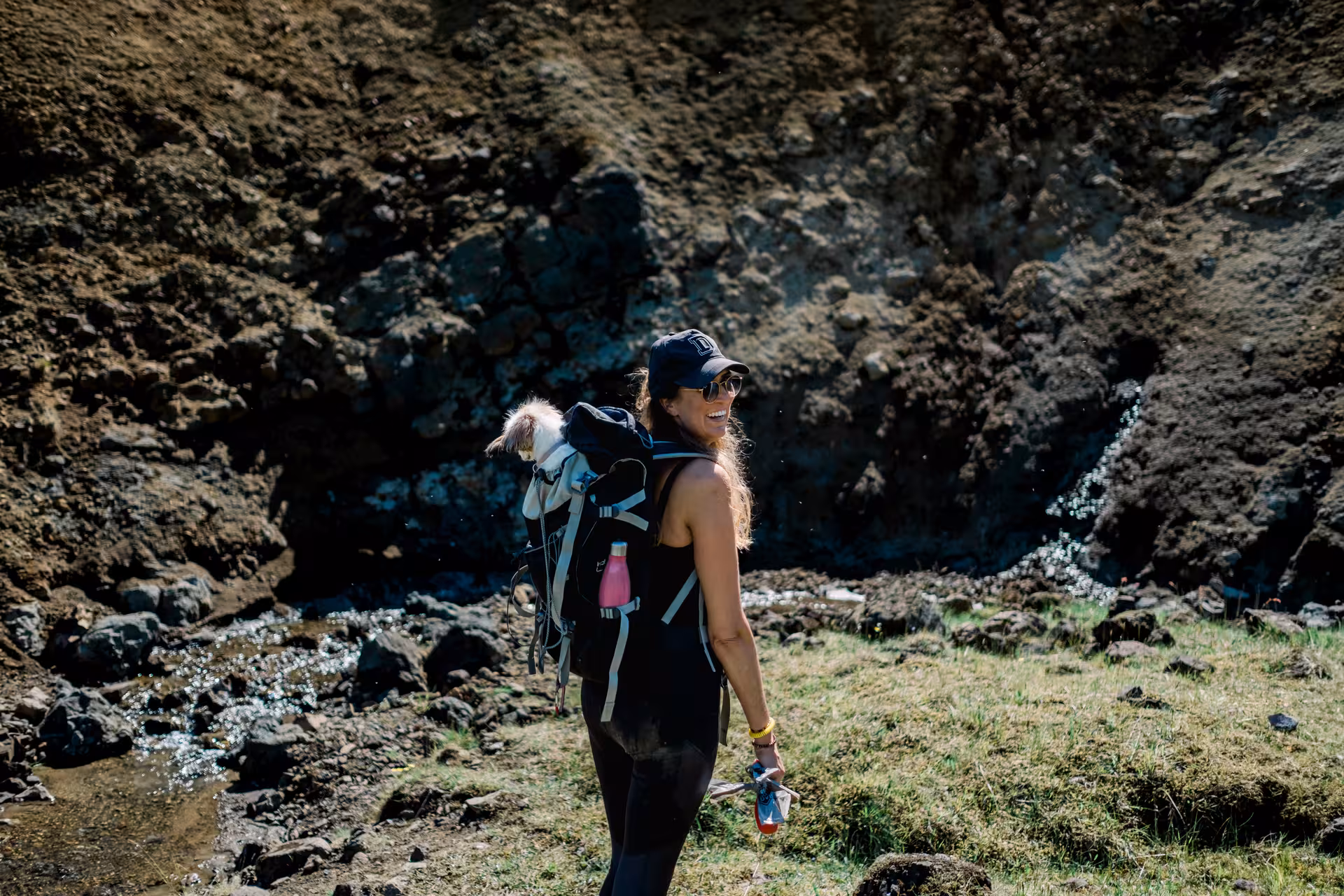 Smiling woman hiking with dog in backpack carrier near Iceland geothermal rocky valley