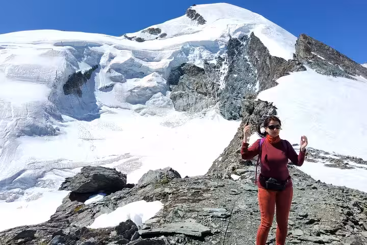 Hiker on rocky ridge below a glacier and snow summit, scenic Swiss Alps day trip from Zurich to Zermatt