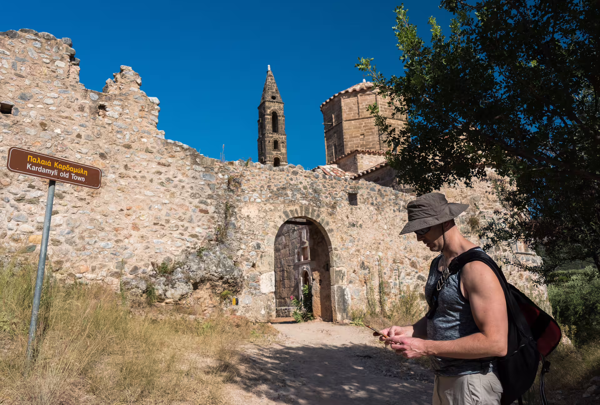 Hiker at Kardamyli Old Town stone gate, Mani Peninsula, Greece, on a guided hiking tour route