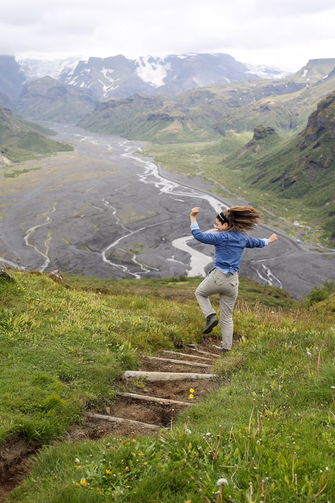 A hiker joyfully leaping on a trail in Thorsmork valley with braided glacial rivers and snow-capped mountains behind.
