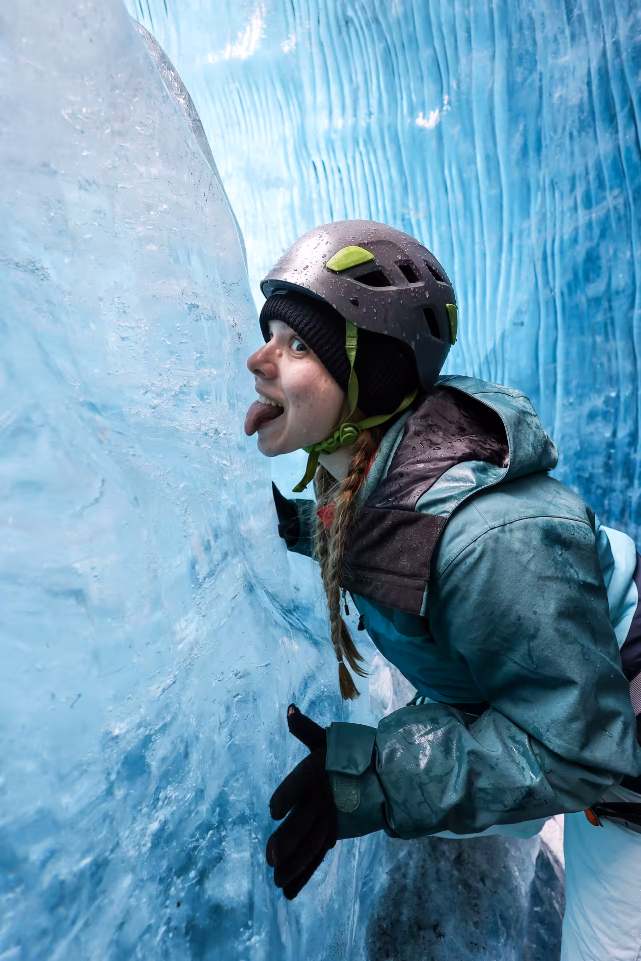 A playful hiker in a helmet licking the ancient blue ice wall during a guided Falljokull glacier hike with photo shoot
