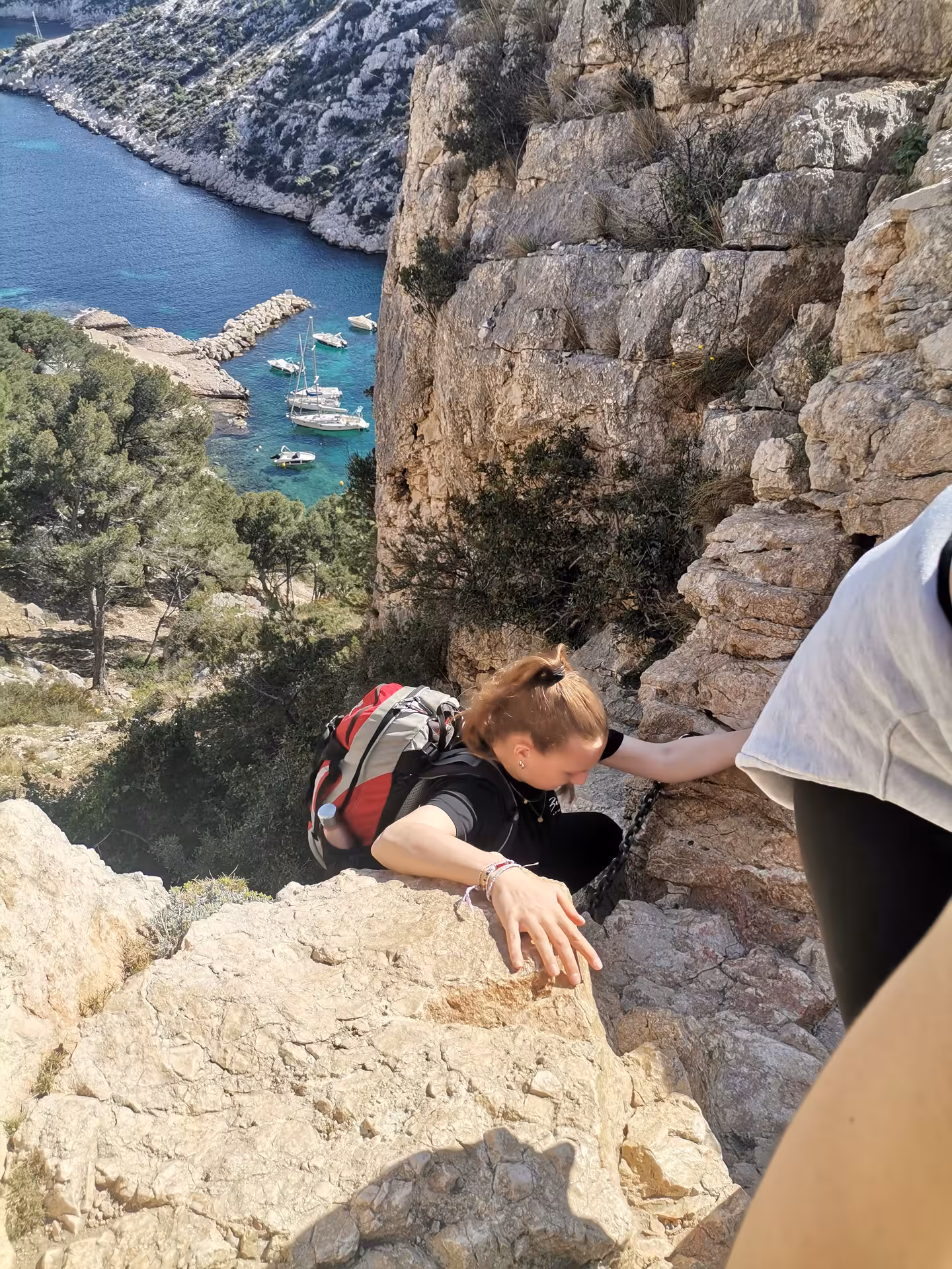 Hiker scrambling on limestone cliff above turquoise Calanques cove, Provence coastal hike on 14-day getaway