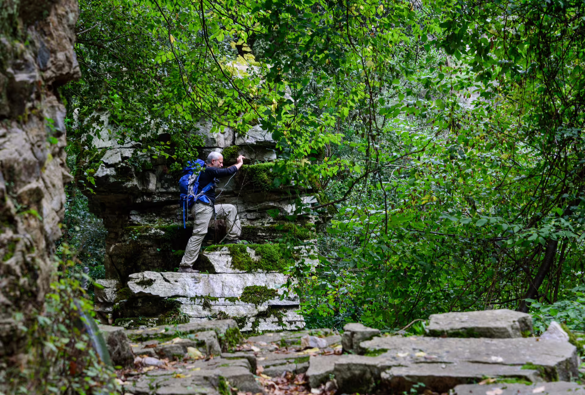 Hiker climbs mossy rock ledge in Ridomo Gorge, Taygetos, exploring a rugged canyon trail on a guided trek