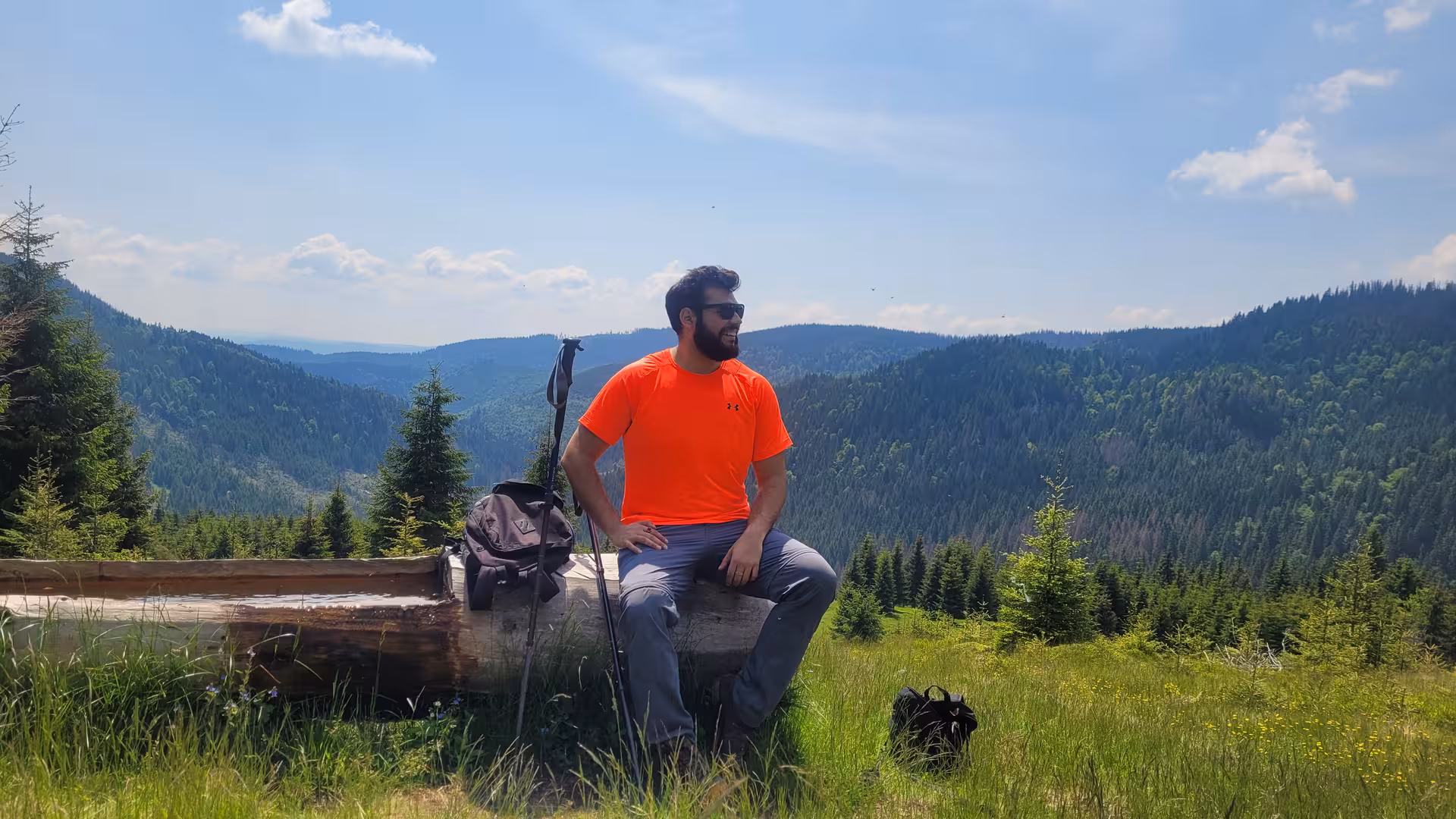 Hiker in orange shirt resting on log at Apuseni mountain viewpoint with forested valley panorama