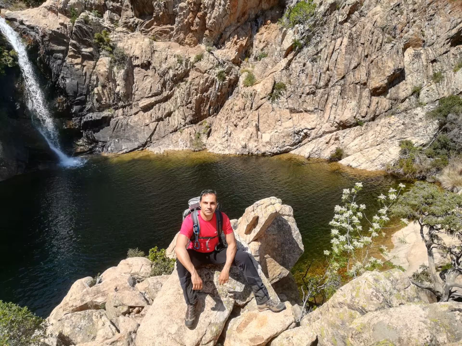 Hiker resting by the scenic Rio Pitrisconi waterfall surrounded by rocky cliffs on the San Teodoro trek.