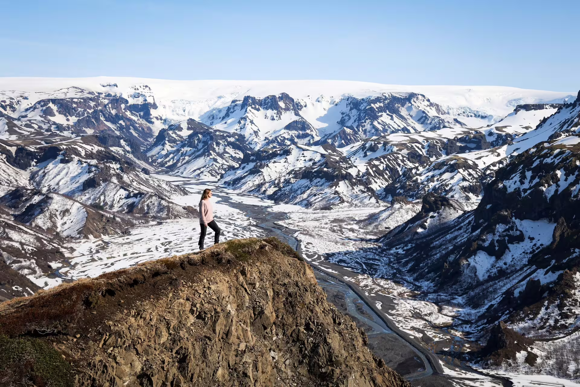 Hiker standing on rocky summit overlooking snowy Viking Valley with sweeping glacier views on Iceland South Coast tour